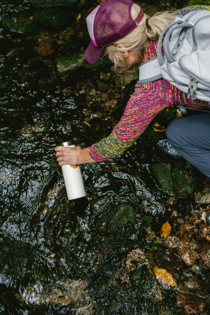 A woman kneels to fill her water bottle from a clear mountain stream while hiking in Patagonia.