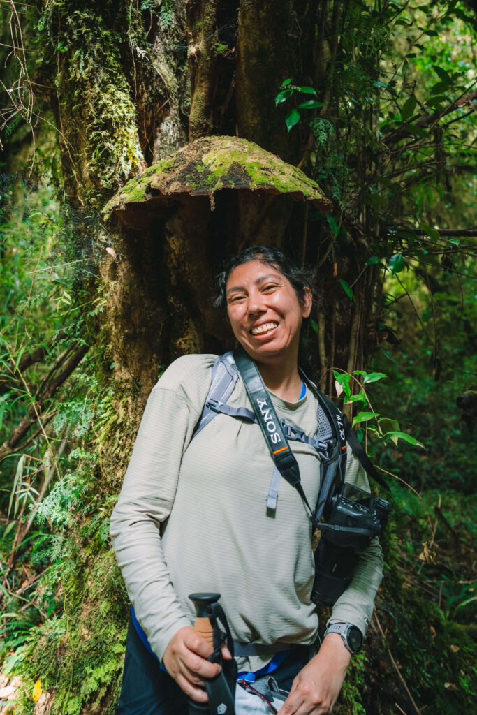 A smiling hiker with a camera stands beneath a large shelf fungus on an old-growth tree in Patagonia.