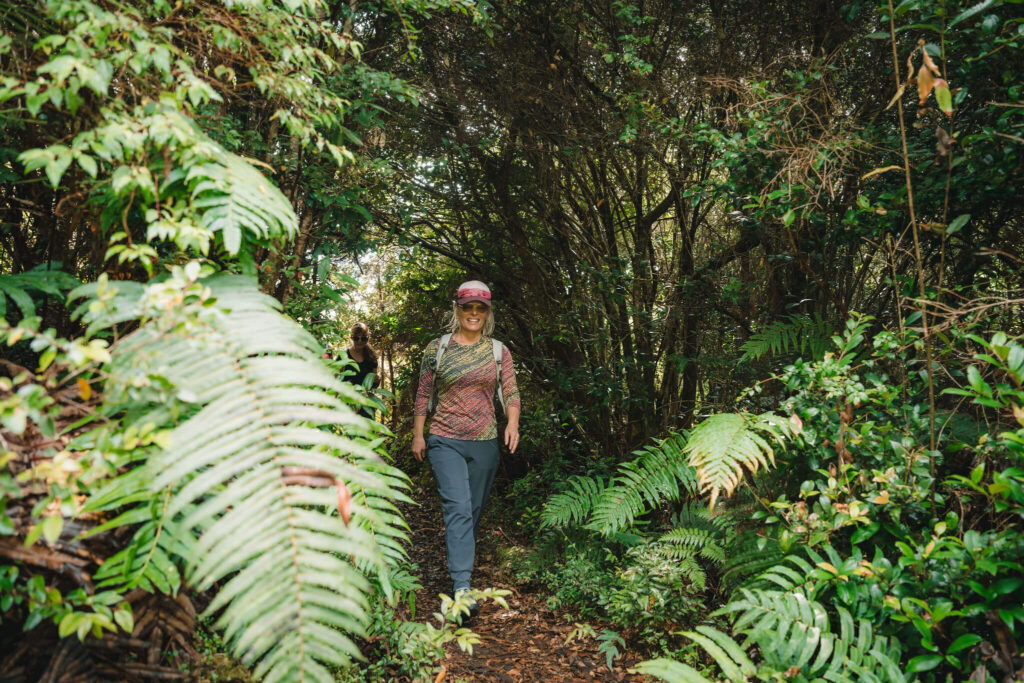 Two women hiking a fern-lined rainforest trail on a women's yoga retreat in Patagonia, Chile.